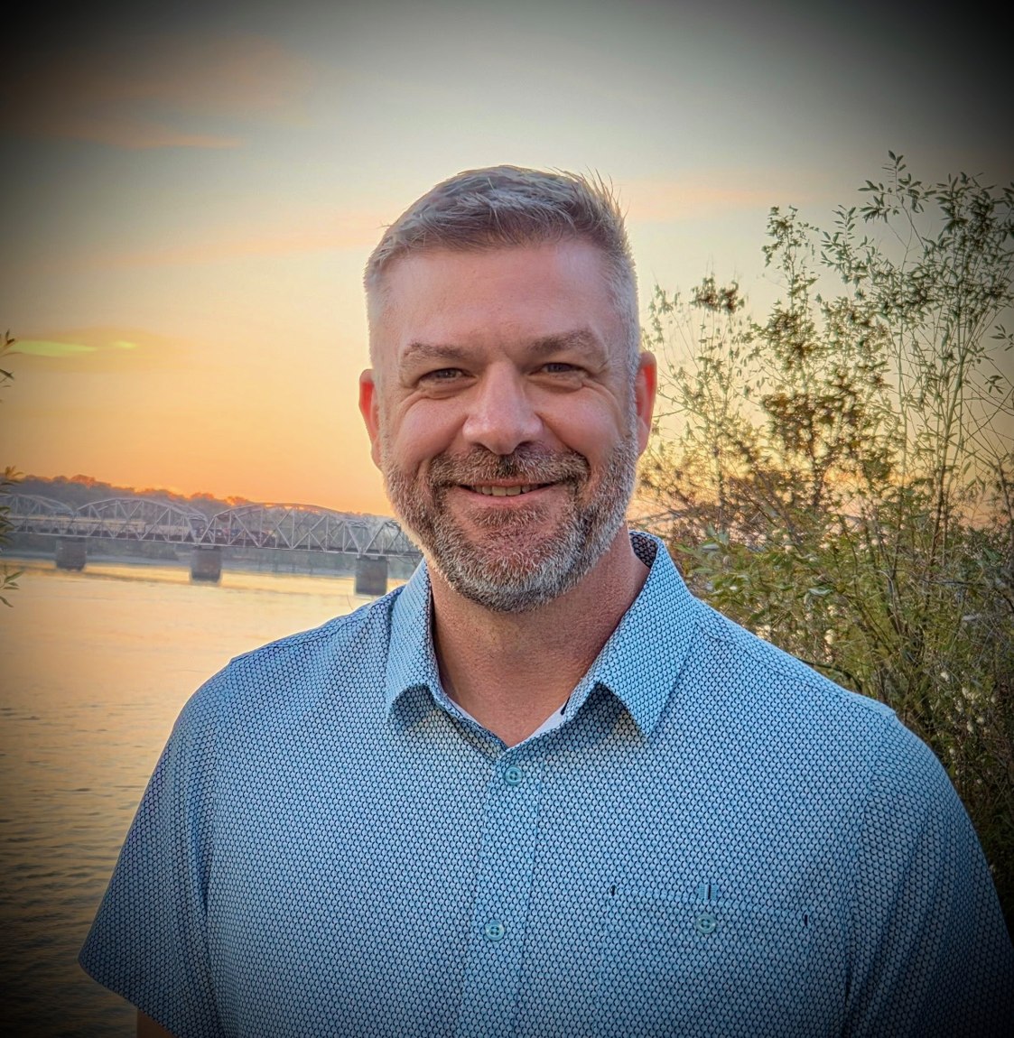 Brian Elerick, owner of High Current Electric, outdoors by the river at sunset